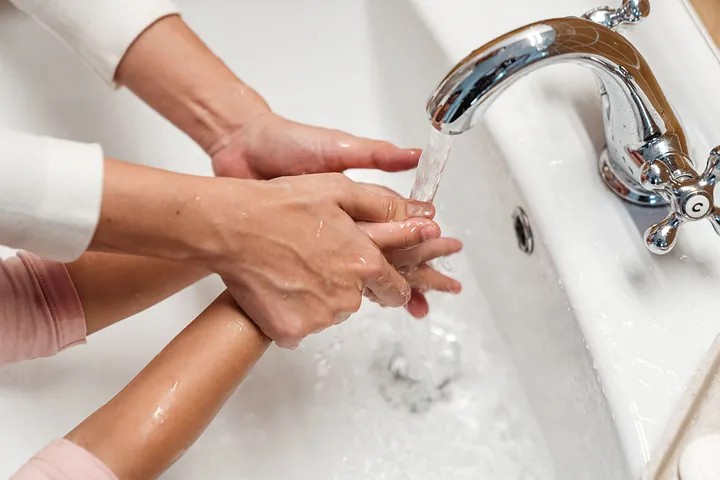 Mãos a lavar-se debaixo de uma torneira, com água corrente.