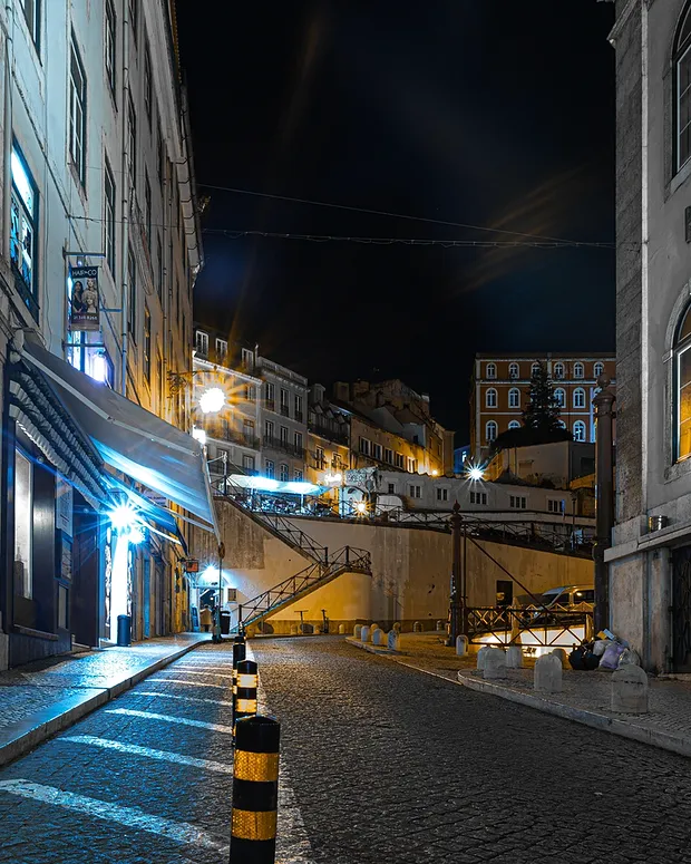 Rua estreita de uma cidade à noite, com candeeiros acesos, fotografia provisória.