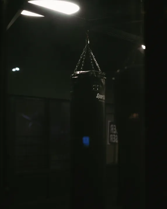 Saco de boxe pendurado numa sala com pouca luz, fotografia provisória.