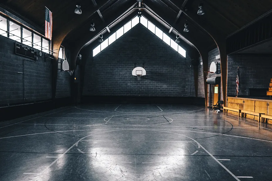 Sala de treino vazia, com vigas no tecto e as luzes acesas ao fundo, fotografia provisória.