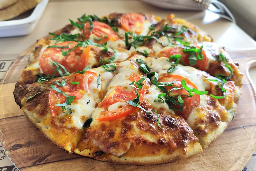 Pizza margherita acabada sobre uma tábua de madeira