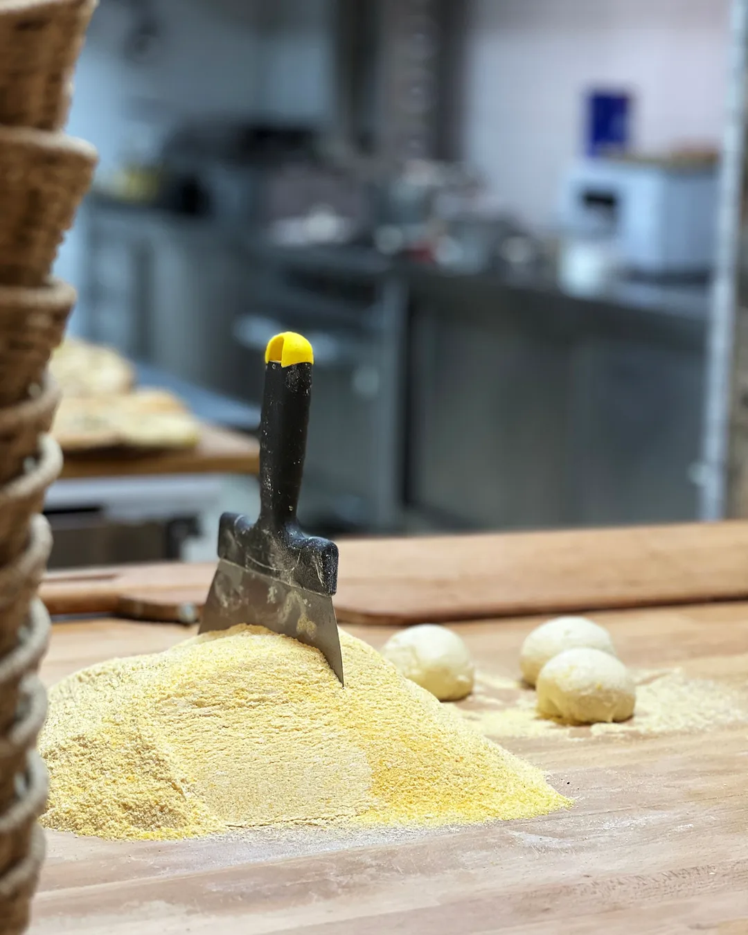Massa de pizza a ser aberta à mão, com farinha e uma espátula na bancada