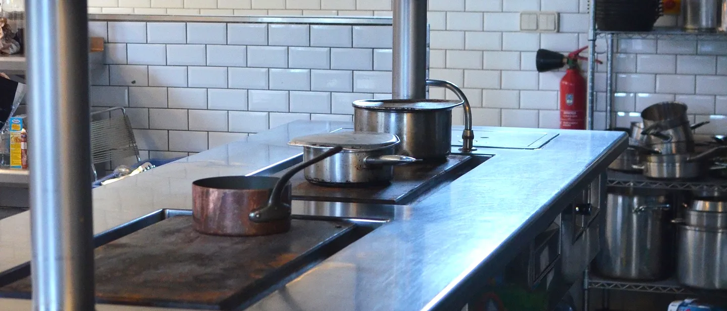 Bancada de aço e azulejo branco numa cozinha aberta.