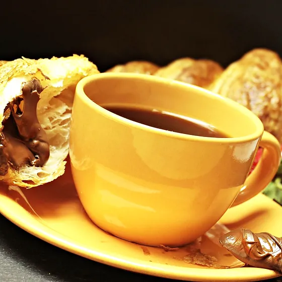 Croissant partido a meio ao lado de uma caneca amarela de café, fotografia provisória.