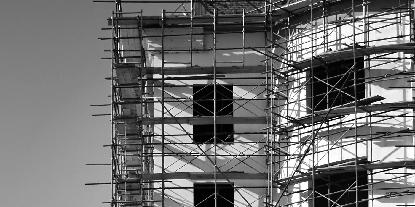 Estrutura de betão em construção, vista de baixo, com andaimes ao fundo.
