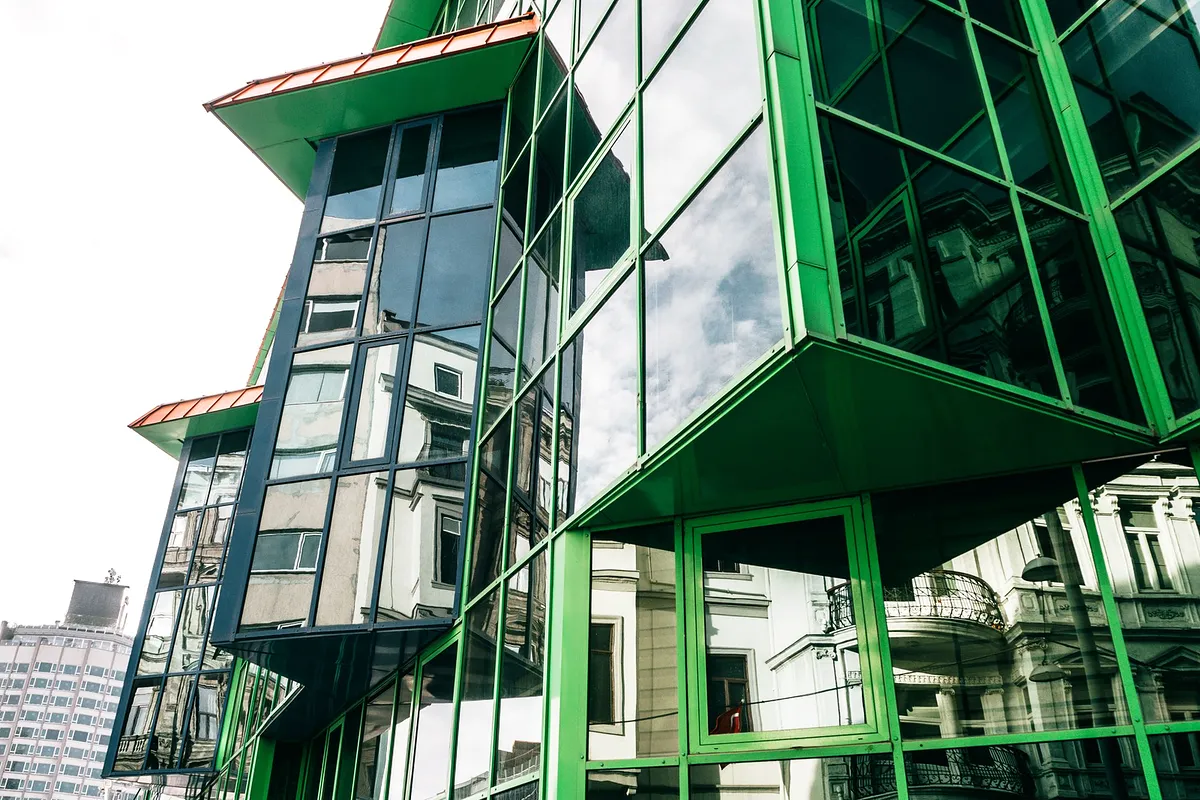 Fachada de vidro verde de um edifício, com a cidade refletida nos painéis.