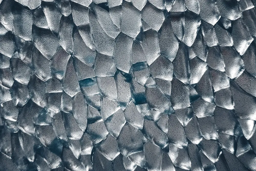 Fachada de vidro com uma textura cristalina, em planos facetados que refletem a luz, sem tratamento de cor.