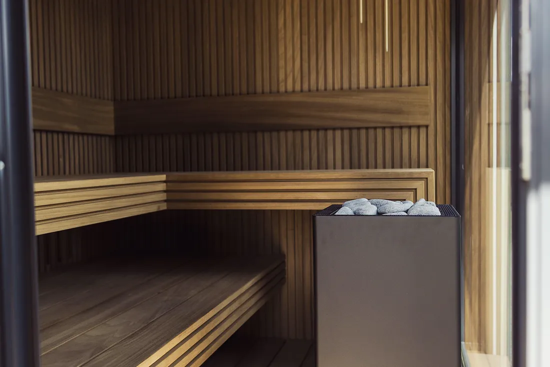 Interior de uma sauna de madeira, com bancos a dois níveis e uma janela pequena.