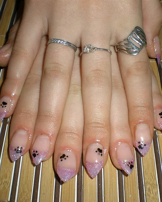 Unhas amendoadas em nude com pequenos desenhos pretos na ponta.