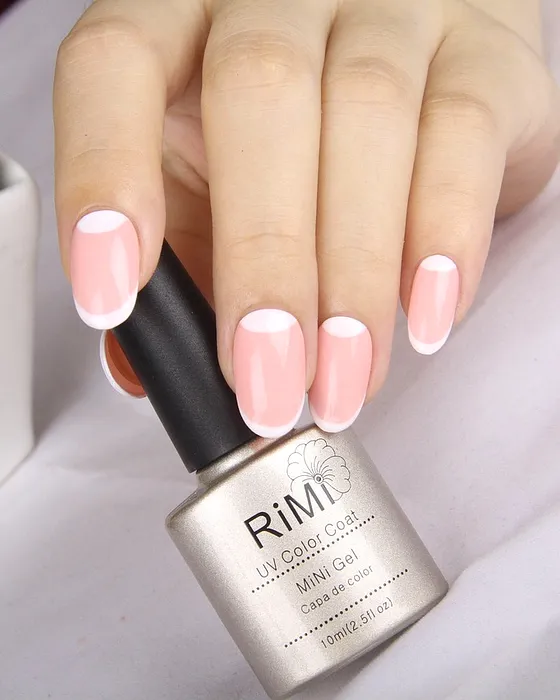 Francesa em rosa claro sobre unha curta, com o frasco de gel na mão.