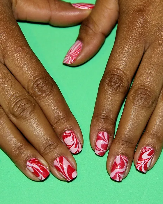 Unhas com marmoreado vermelho e branco sobre pele escura.