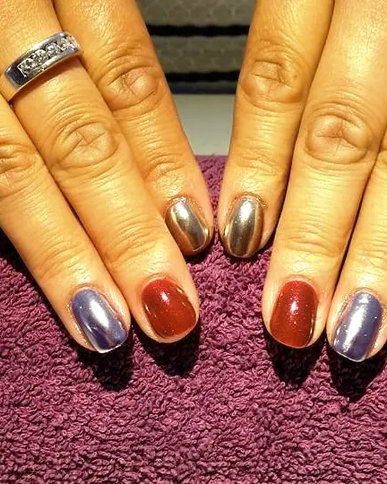 Unhas alternadas em vermelho escuro e cromado sobre um tecido ameixa.
